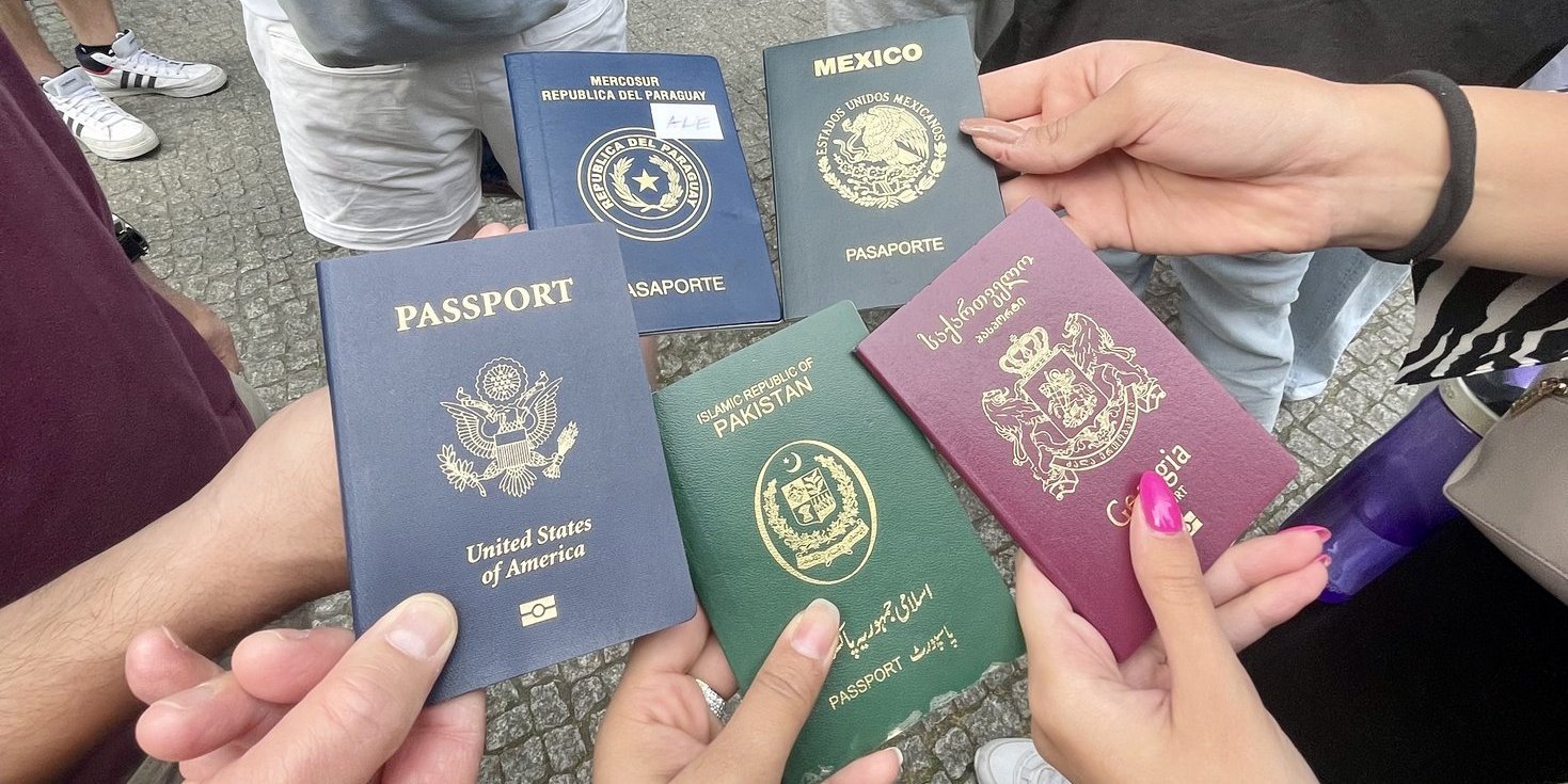 Students are holding six different passport covers into the camera (Paraguay, Mexico, USA, Pakistan, Georgia)